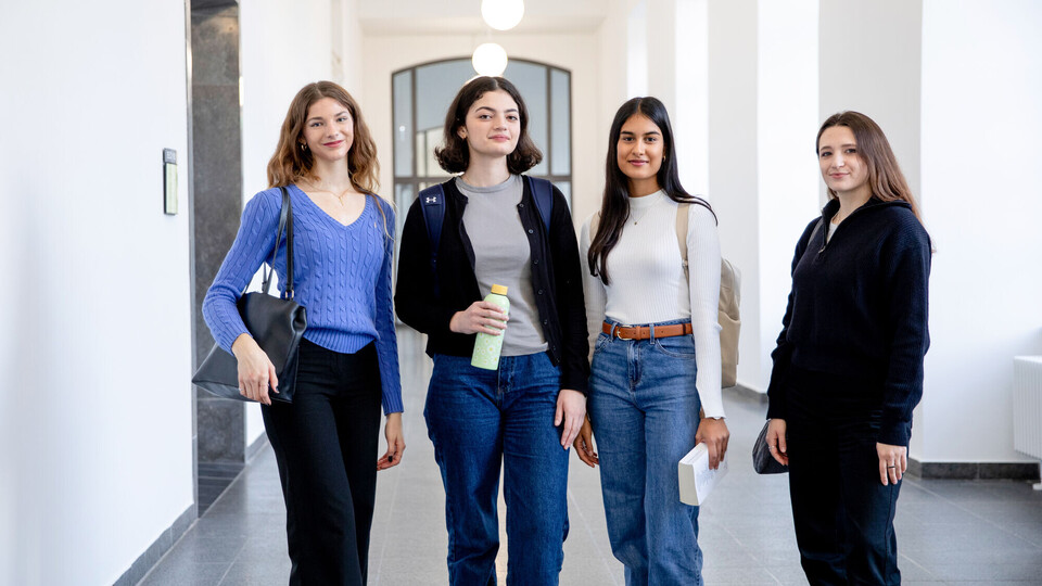 Vier junge Frauen stehen in einem weiß gestrichenen Flur des Mannheimer Schlosses. Sie schauen selbstbewusst in die Kamera.