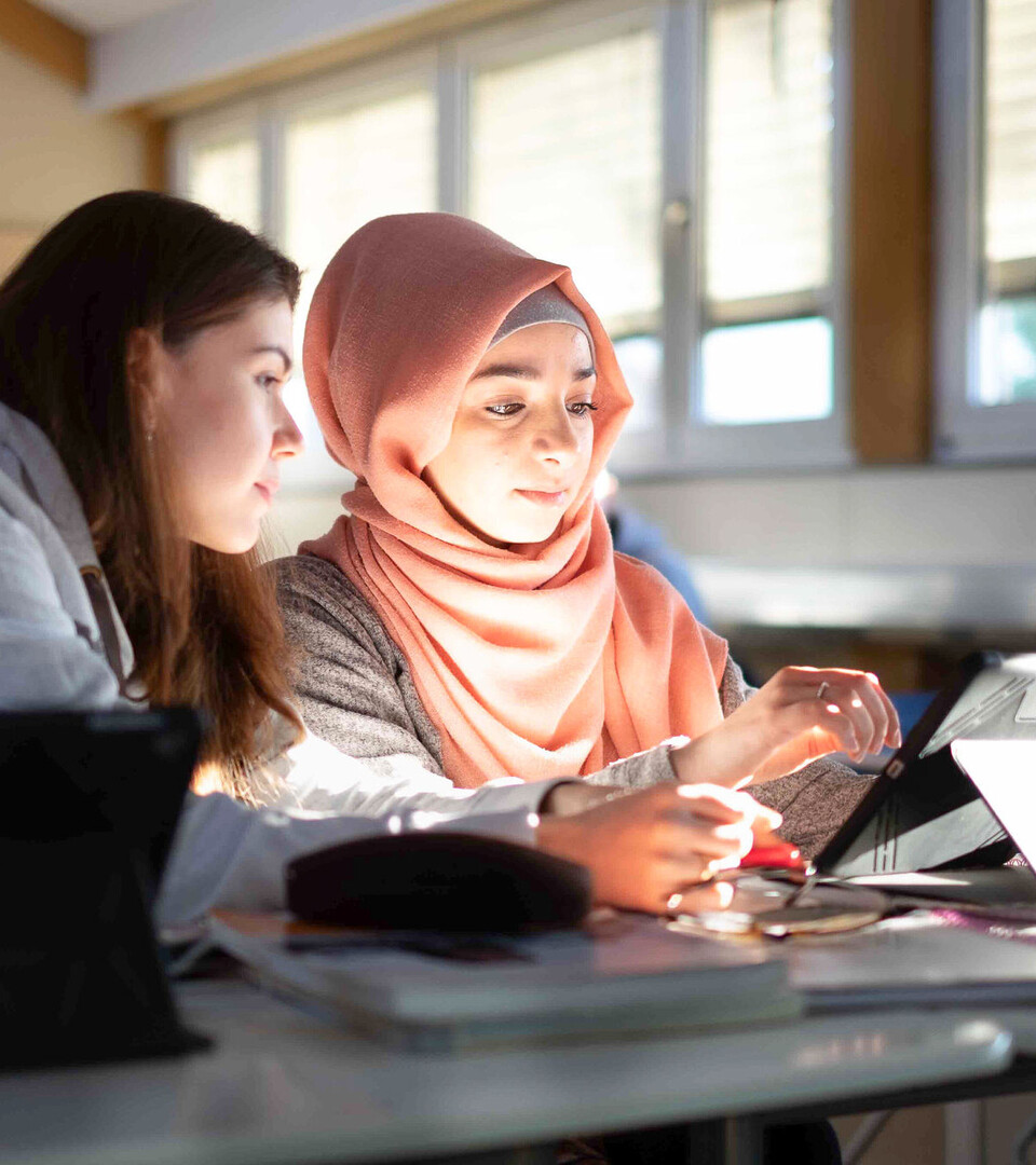 Lehrerausbildung Zwei Studentinnen sitzen an einem Tisch. Eine Studentin trägt ein Kopftuch.